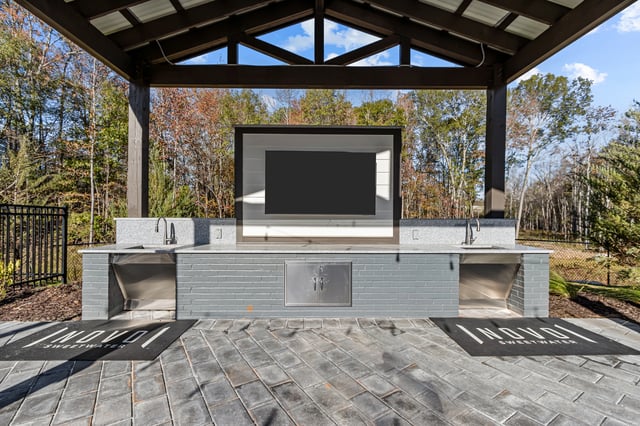 Outdoor kitchen area with sinks, countertops, and a large screen television mounted above.
