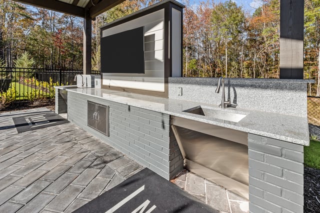 Outdoor kitchen with sink, countertops, and a television.