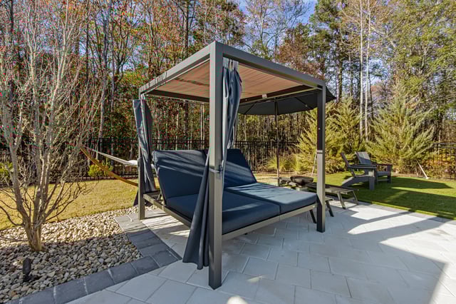 Outdoor daybed with canopy and curtains, hammock, and chairs in a grassy courtyard.