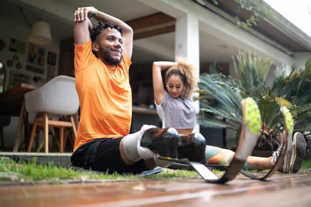 A man and woman with prosthetic legs stretching outdoors.