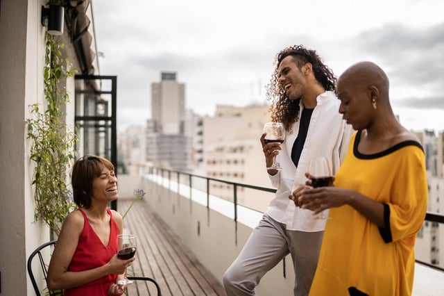 Three friends enjoying wine on a balcony with a city view.