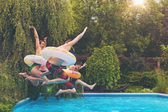 People jumping into a swimming pool with inflatable rings.