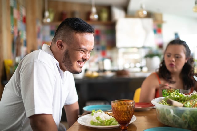 A man with Down syndrome smiling while sharing a meal with a woman.