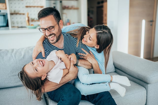 A happy family laughing and playing together on a sofa.