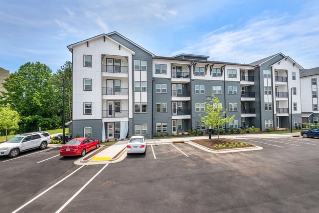 Exterior view of a modern apartment building with a parking lot and trees.