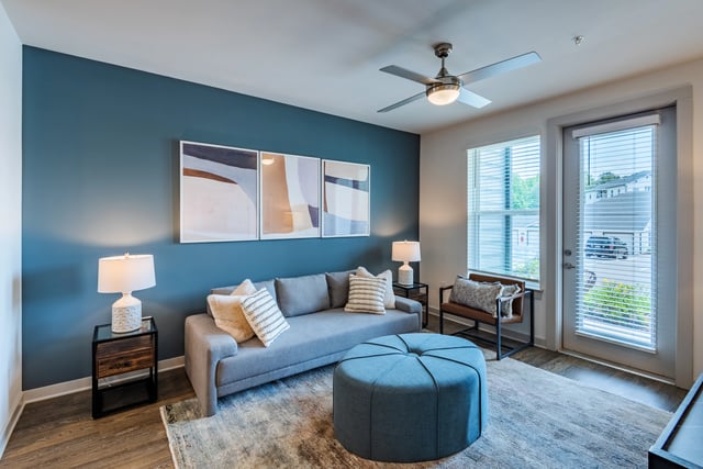 A living room with a gray sofa, blue ottoman, and abstract art.
