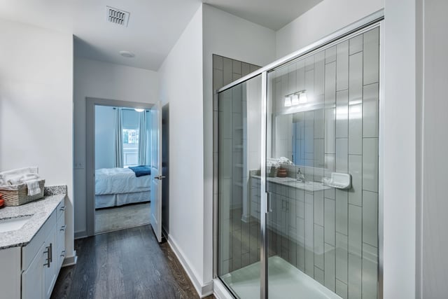 Modern bathroom with double vanity, shower, and view of bedroom.