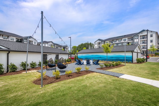 Courtyard with fire pit, Adirondack chairs, hanging chairs, and string lights at apartment complex.