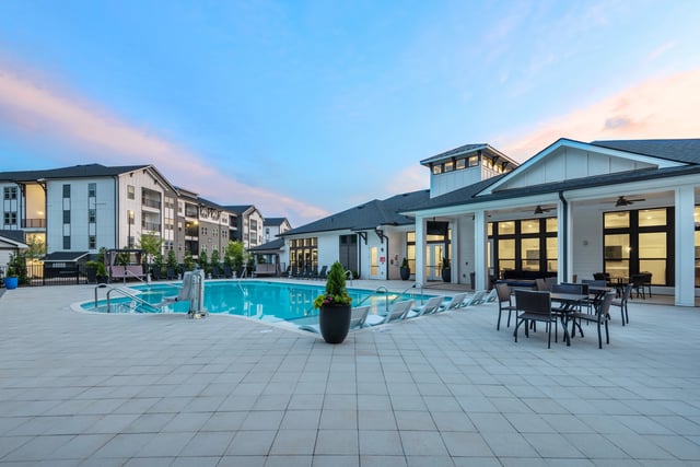 Outdoor swimming pool and lounge area with apartment buildings in the background.