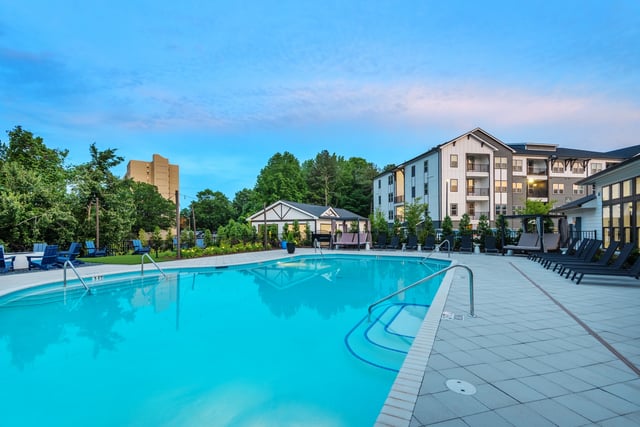 Outdoor swimming pool with lounge chairs and cabana at dusk.