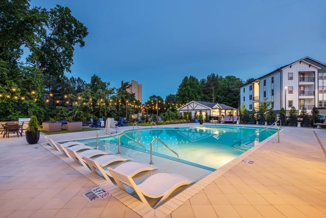 Outdoor swimming pool with lounge chairs and string lights at dusk.
