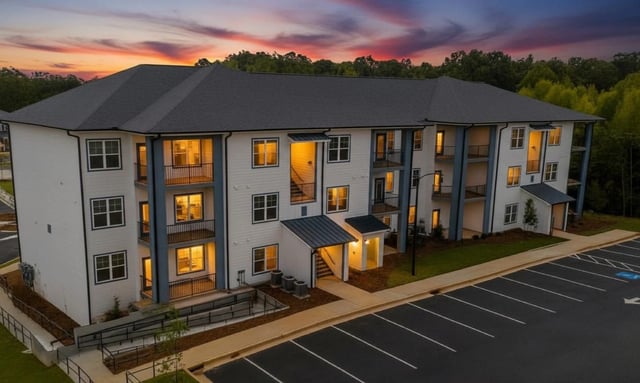 Exterior view of a modern apartment building at dusk with warm lights glowing from windows and balconies.