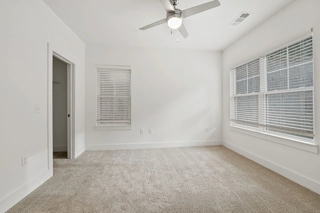 Empty bedroom with neutral carpet, ceiling fan, and large windows with blinds.