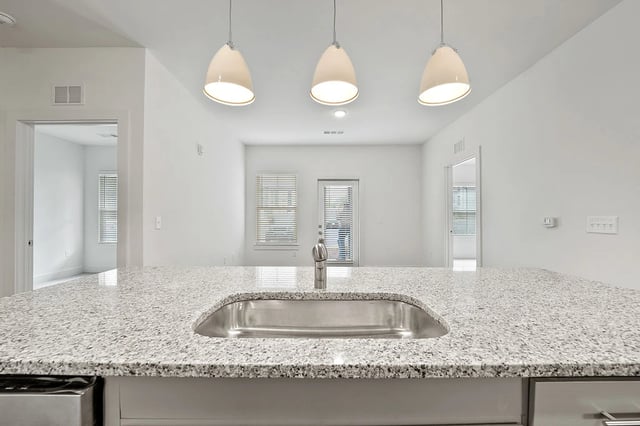 Modern kitchen with granite countertops, stainless steel sink, and pendant lights.