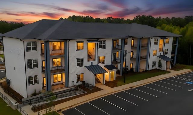 Exterior of a modern apartment building at dusk with lights on in the windows and balconies.