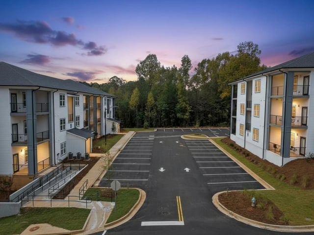 Exterior view of apartment buildings with parking lot and trees at dusk.