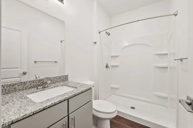 Modern bathroom with granite countertop, vanity, toilet, and shower.