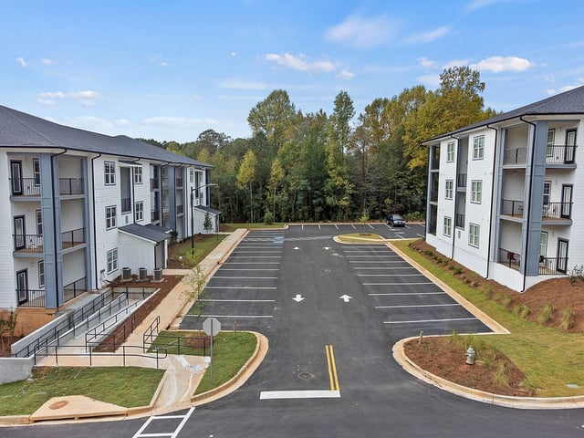 Modern apartment buildings with a large parking lot and surrounding greenery.