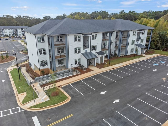 Exterior of a modern apartment building with a large parking lot in front.