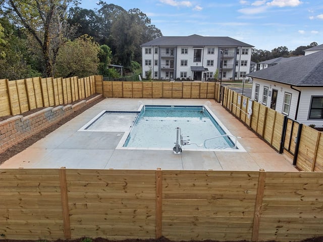 Outdoor swimming pool with a tanning ledge, surrounded by a wooden fence.