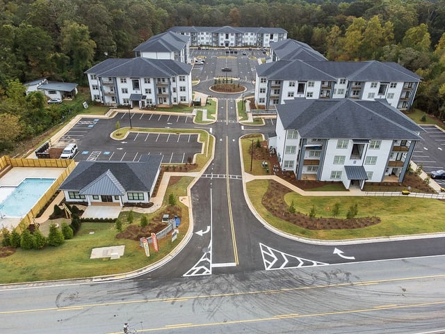 Aerial view of a new apartment complex with multiple buildings, a swimming pool, and a clubhouse.