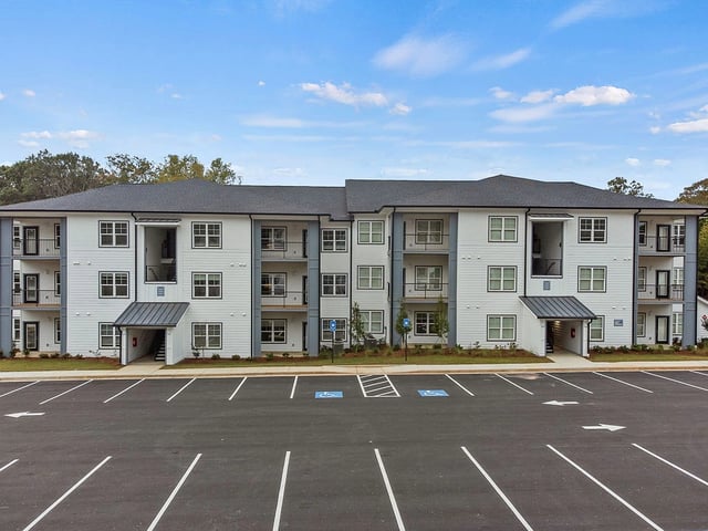 Exterior of a multifamily apartment building with balconies and a parking lot.