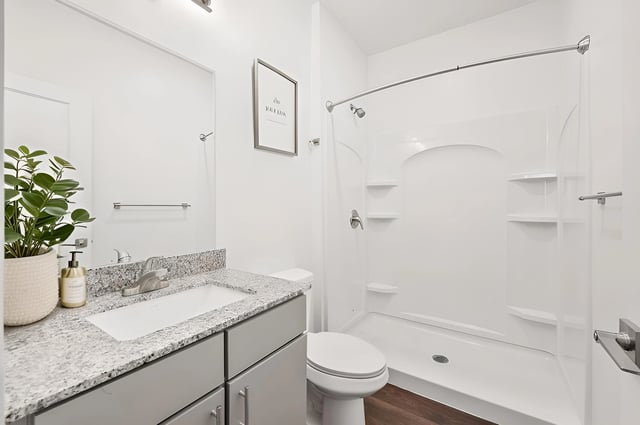 Modern bathroom with a granite countertop vanity, stainless steel faucet, and a walk-in shower.