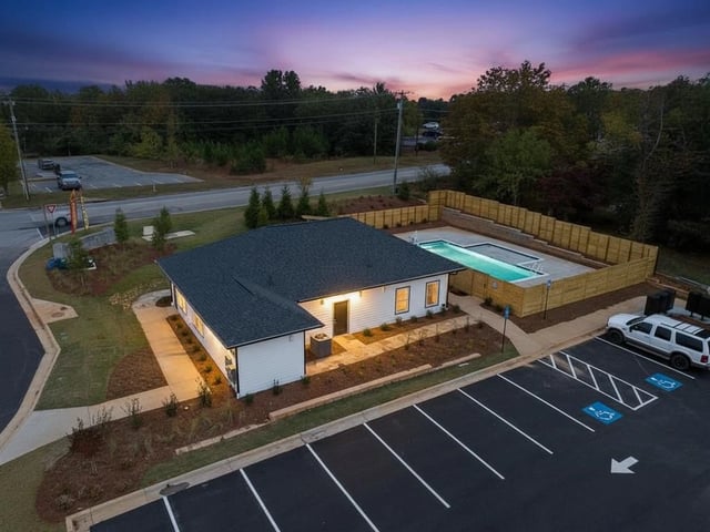Aerial view of a white building with a pool and parking lot at twilight.