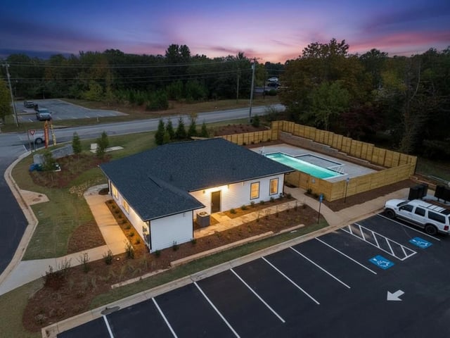 Exterior view of the property with a pool and parking lot at dusk.