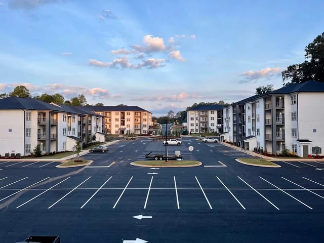 Exterior view of apartment buildings with a large parking lot in front.