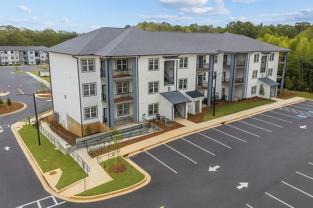 Exterior view of a multifamily apartment building with a large parking lot.