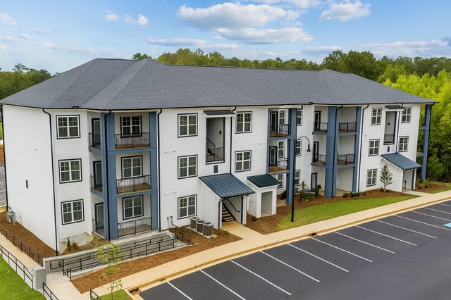 Exterior of a modern apartment building with white siding and blue trim, featuring balconies and a parking lot.