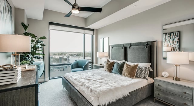 Modern bedroom with a king-size bed, large window with city view, and plush furnishings.