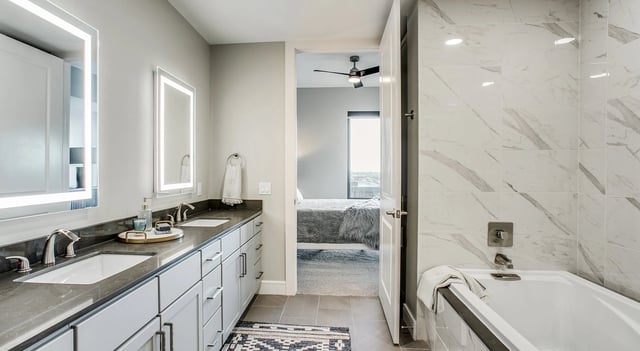 Modern bathroom with double vanity and soaking tub, view of bedroom beyond.