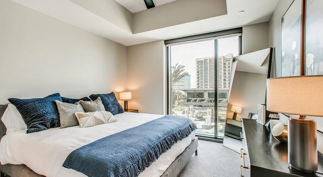 Modern bedroom with king-size bed, large mirror, and city view.