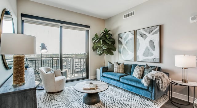 Modern living room with blue velvet sofa, armchair, and balcony access.