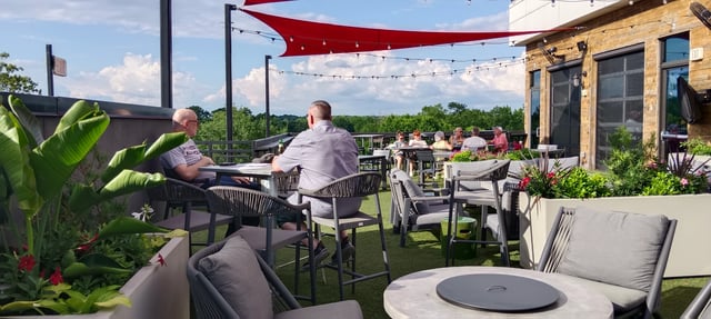 Rooftop patio with seating, umbrellas, and people dining outdoors.