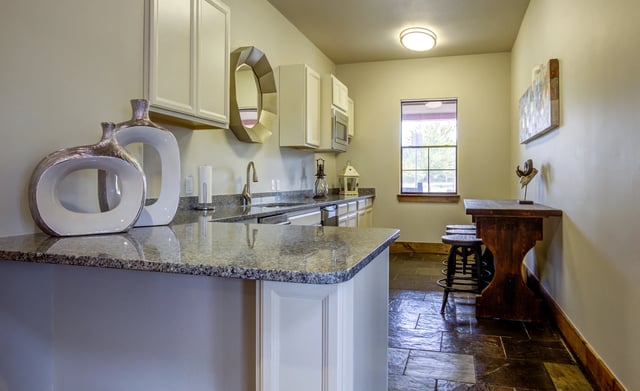 Kitchenette with granite countertops, white cabinets, and a sink.