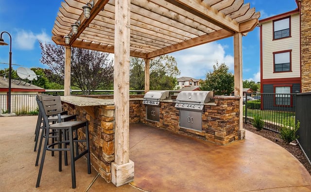 Outdoor kitchen with two grills and bar seating under a wooden pergola.