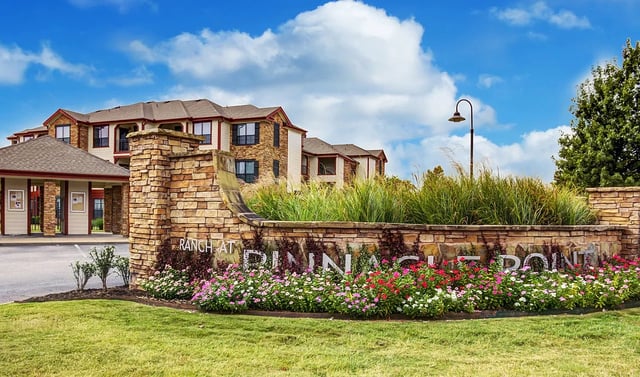 Ranch at Pinnacle Point monument sign with landscaping and apartment buildings in the background.