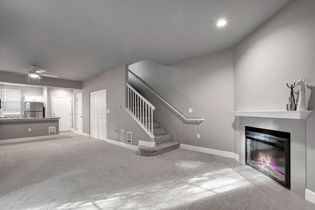 Interior living area with staircase, fireplace, and open kitchen in a neutral-toned apartment.