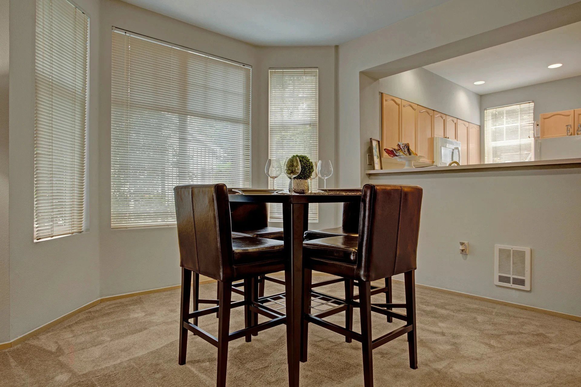 Dining area with a high table and four brown leather chairs beside a kitchen pass-through.