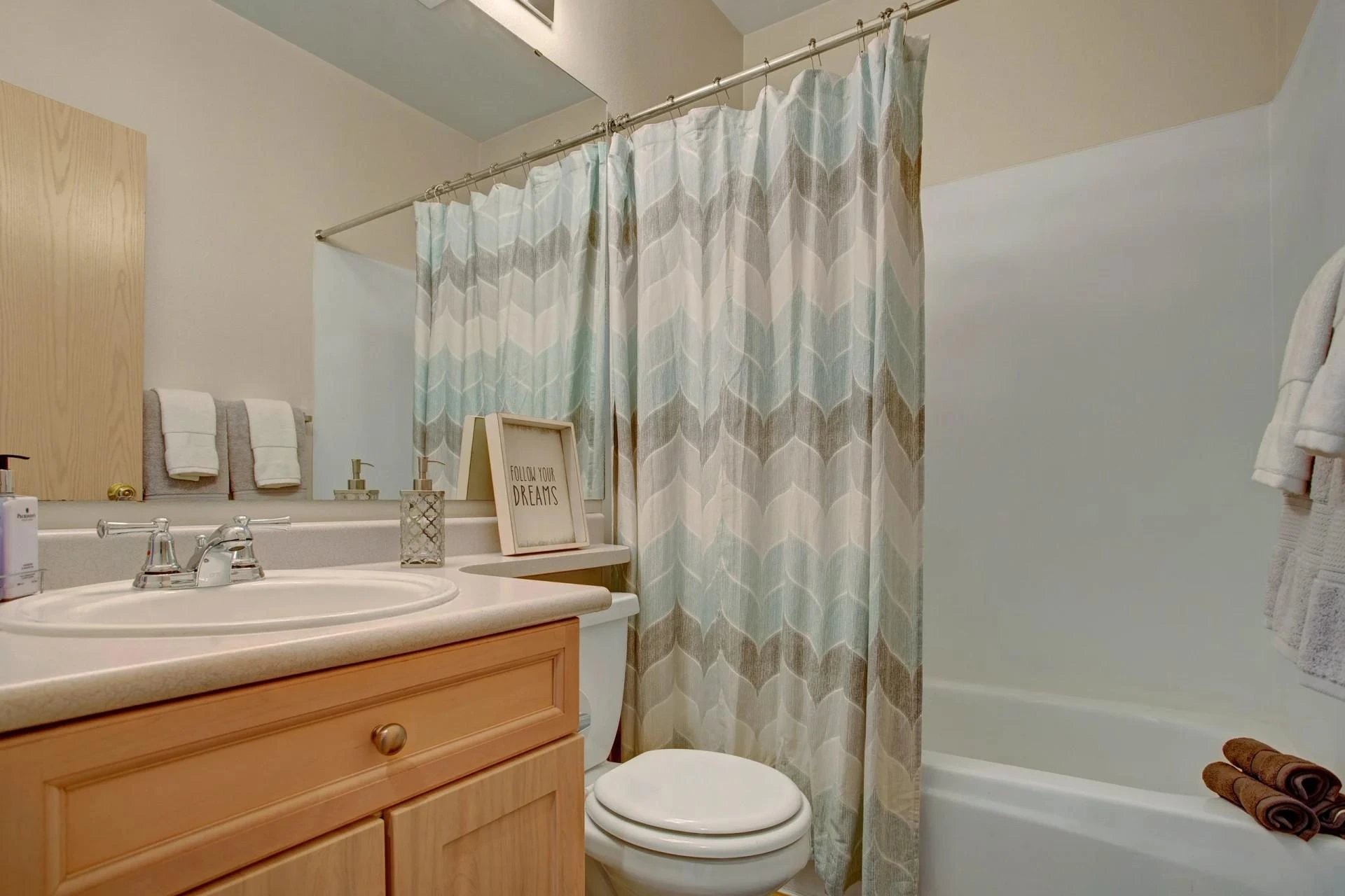 Bathroom in an apartment with vanity, sink, mirror, toilet, and patterned shower curtain.