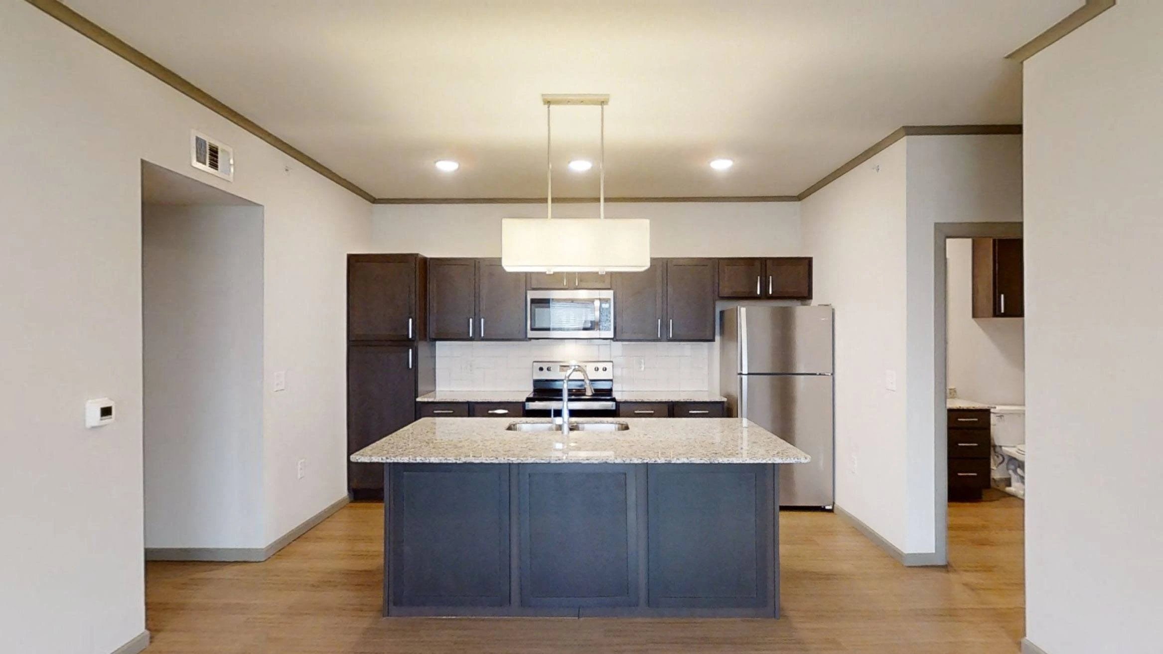 Modern kitchen with island, granite counters, dark cabinets, and stainless steel appliances.