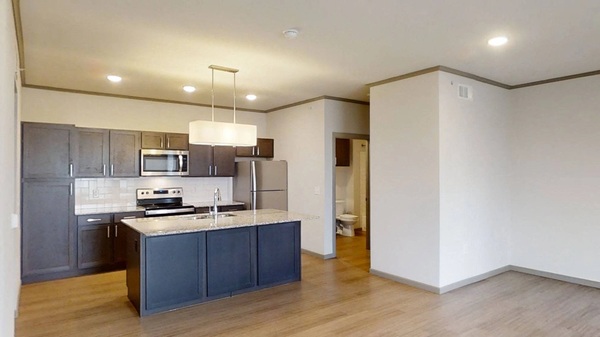 Open-concept kitchen with dark cabinetry, stainless steel appliances, and a granite island.