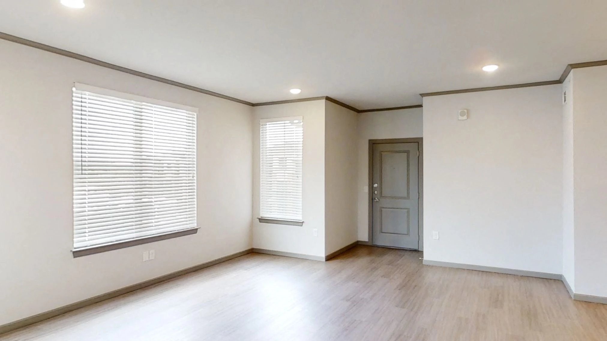 Empty living area with two large windows and blinds.