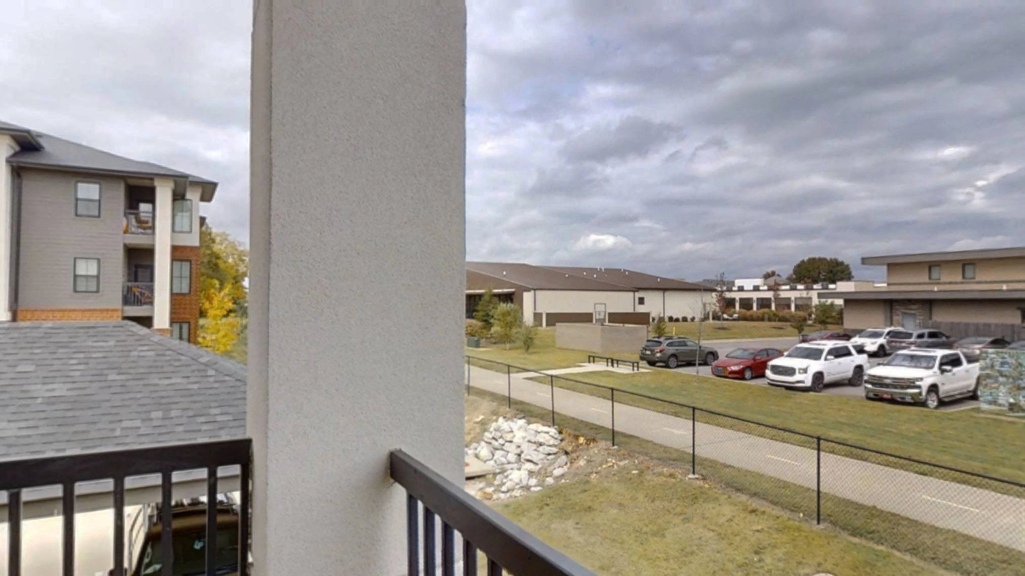 Balcony view of a modern apartment complex with a parking lot and grassy courtyards.