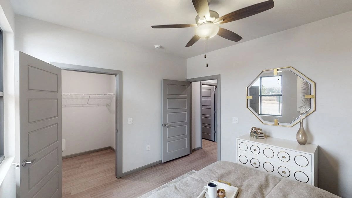 Bedroom in an apartment with a ceiling fan, bed, dresser, and open closet.
