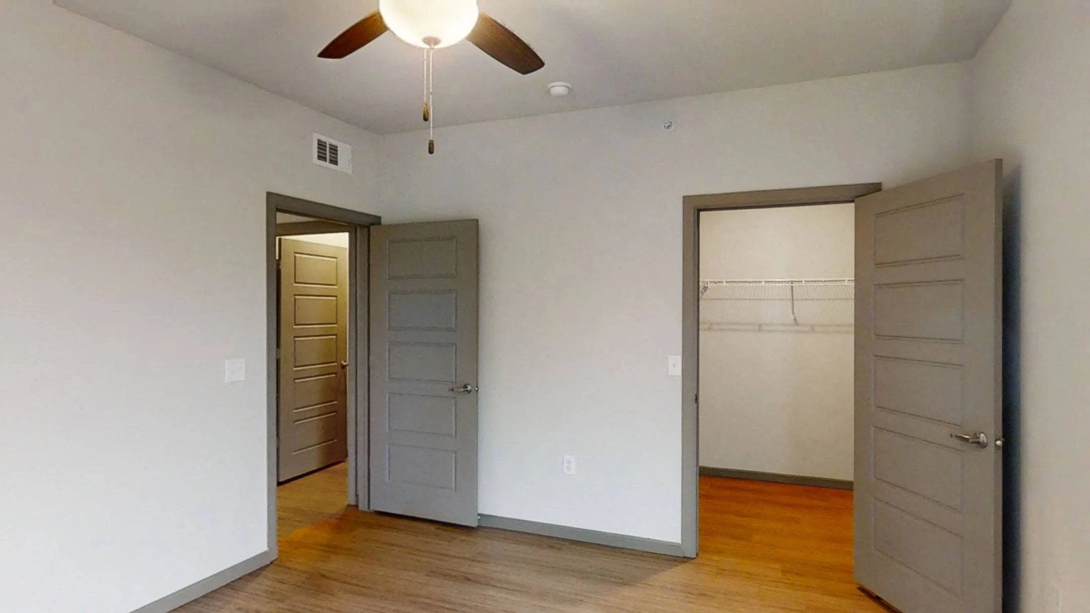 Bedroom with ceiling fan, two gray doors, and a closet with wire shelving.