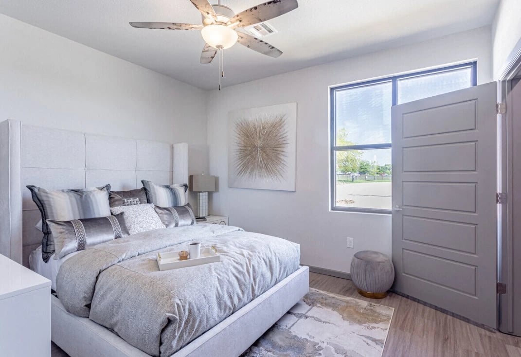 Bedroom with gray upholstered bed, coordinating bedding, two nightstands, and a ceiling fan.
